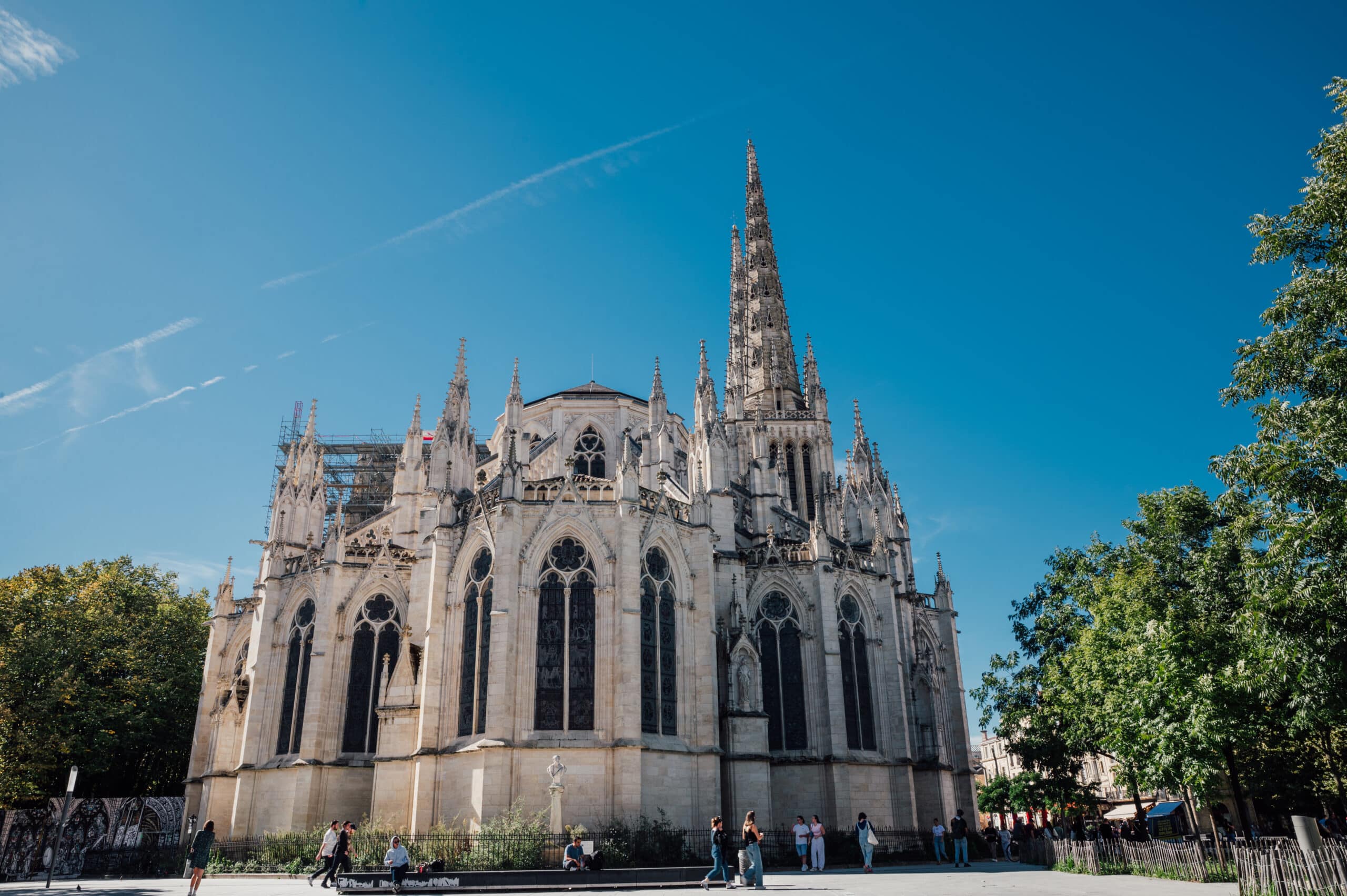 Femme souriante vêtue de noir devant un bâtiment parisien Portrait souriant d'une femme aux cheveux bruns, vêtue d'une veste noire sur une robe violette, devant un bâtiment de style haussmannien.
