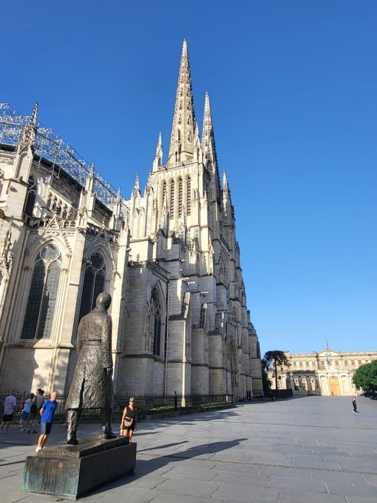 Cathédrale Saint-André et statue Jean-Paul II à Bordeaux Cathédrale Saint-André de Bordeaux, statue de Jean-Paul II et place Pey-Berland sous un ciel bleu.